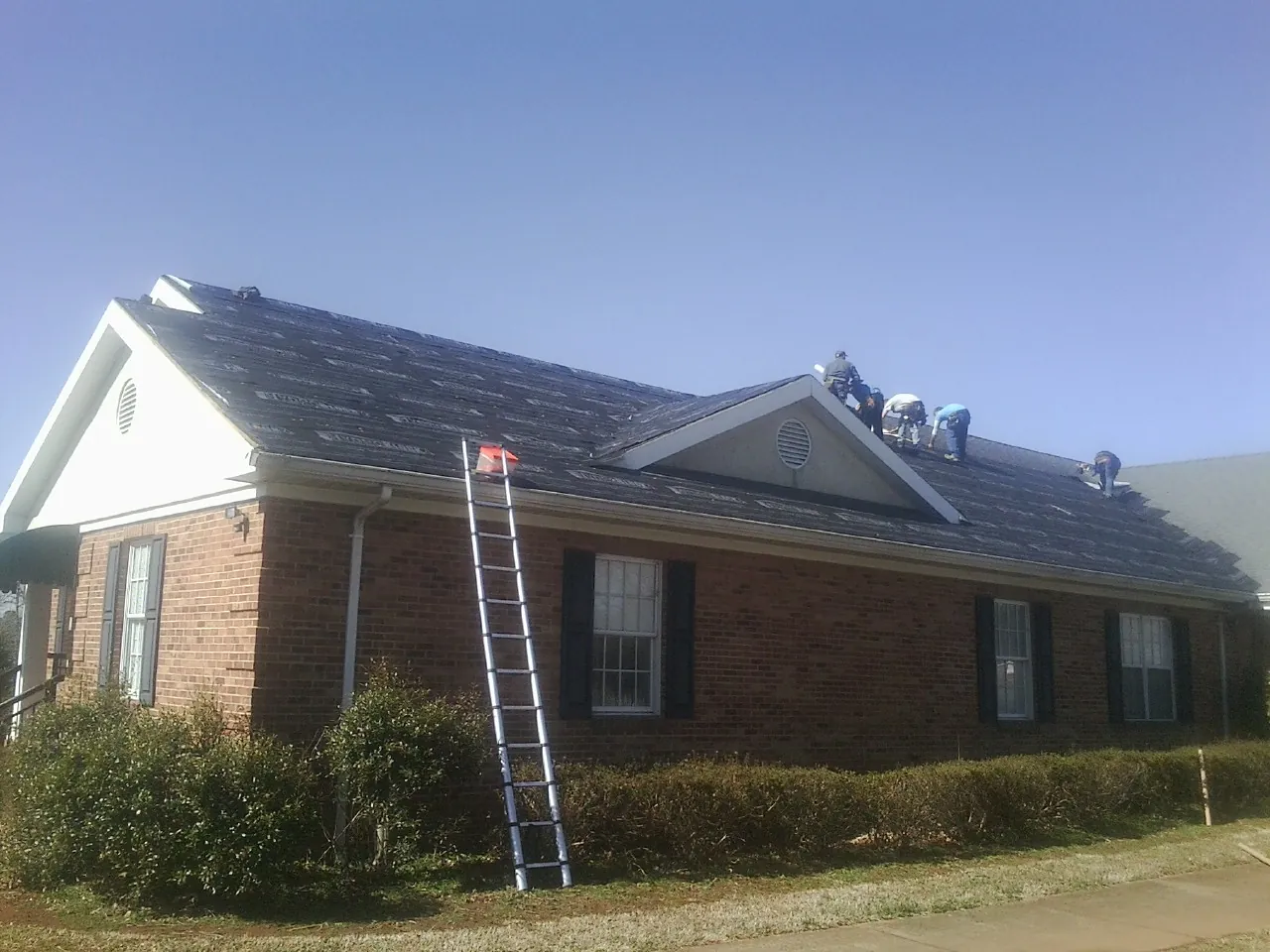 Crew tearing shingles off a brick ranch roof with a ladder set — Emergency Roof Repair work by our crew in Oakman