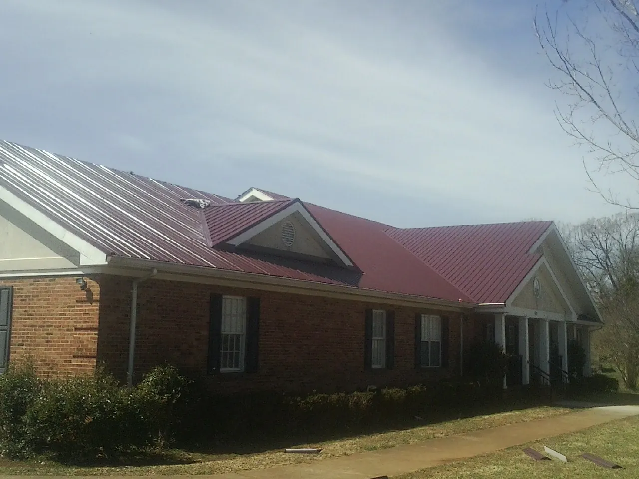 Red metal roof with gabled entries on a long brick building, from a Hail Damage Roof Repair job in Oakman