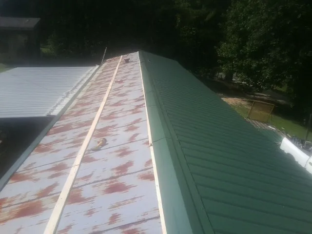 Old rusted panels beside newly installed green metal roofing — Wind Damage Roof Repair by Roofing Brothers in Oakman