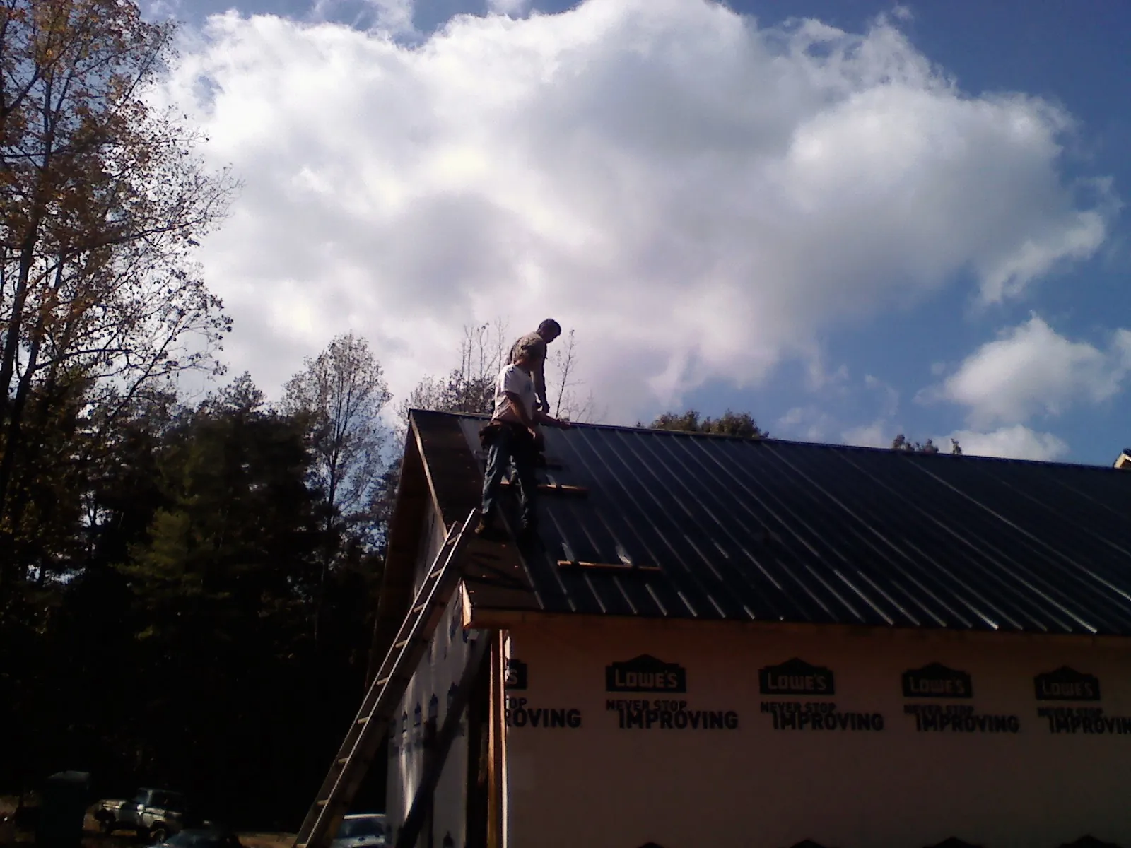 Roofer fastening dark metal panels high against a cloudy sky, from a Roof Inspection job in Oakman