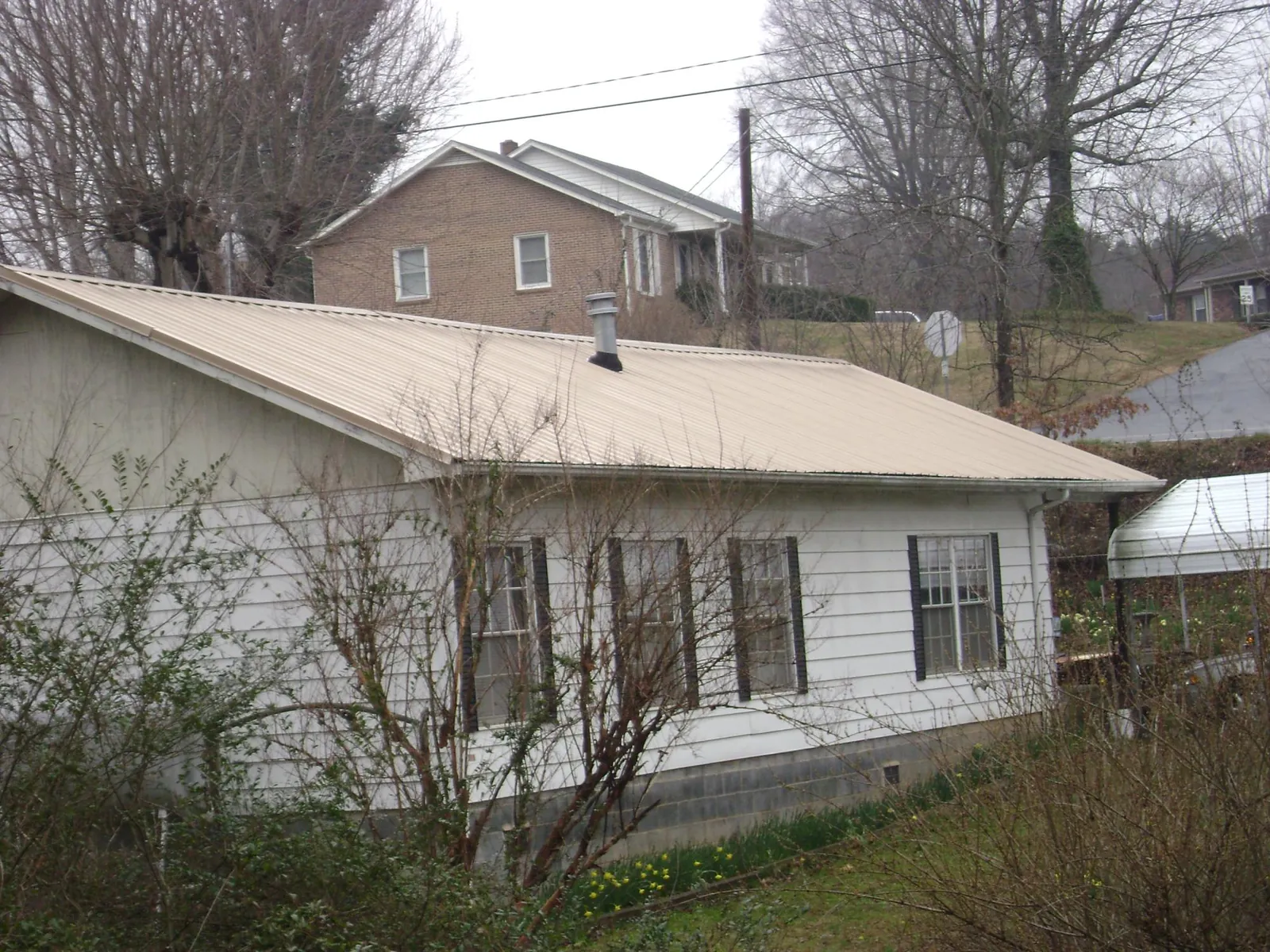 Tan metal roof on a white sided house set into a hillside — Commercial Roofing by Roofing Brothers in Oakman