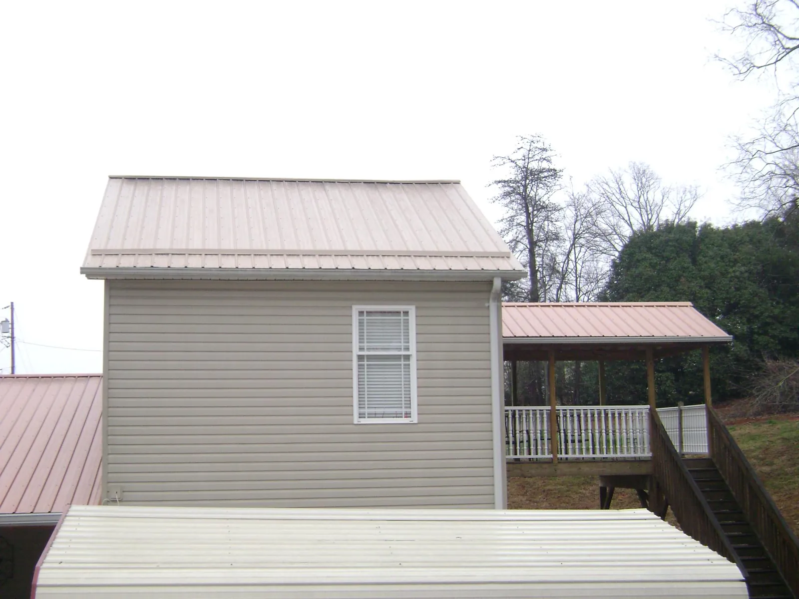 Tan metal roofs on a two story addition and attached porch, from a Roof Replacement job in Oakman